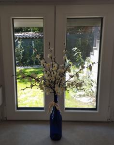 a blue vase with flowers in front of a window at Matróz Lak Apartman in Alsóörs +3 photos