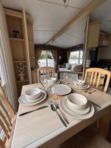 a wooden table with plates and wine glasses on it at Welsh Bay Hideaway 2 bed caravan with sun deck in Aberystwyth