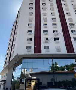 a tall white building with a reflection in the window at Apartamento - Leblon 409 Conforto & Estilo. in Cuiabá
