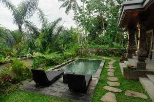 a swimming pool in a garden with two chairs at Wanasari Villa in Tampaksiring