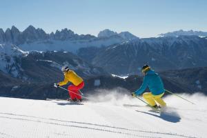 two people are skiing down a snow covered mountain at Hotel Rosental in Luson