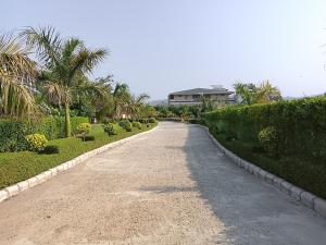 a gravel road with bushes and a house in the background at Corbett Krishna Inn in Belparāo