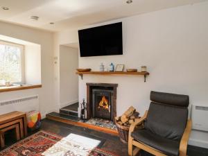 a living room with a fireplace with a chair and a television at Gun Powder Cottage in Tighnabruaich