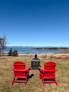 two red chairs and a fireplace in a field at L'Anseau-Persil in Rivière-du-Loup