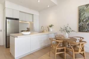 a kitchen with white cabinets and a table with chairs at Azure Horizon - Bay Views & Rooftop Spa in Frankston