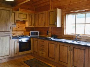 a kitchen with wooden cabinets and a sink and a stove at Sun Rise Lodge No 10 - Hw7655 in Llanbedr