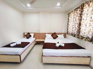 two beds in a room with white walls at Sai Tara Residency in Shirdi