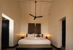 a bedroom with a white bed with a ceiling fan at Fort Tiracol Goa in Arambol