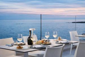 a table with white chairs and wine glasses and the ocean at Hotiday Rooms Torre Pali in Torre Pali