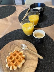 a table with a plate of waffles and two glasses of orange juice at Chalet Des Aigrettes- Jacuzzi privatif in Chassey-lès-Montbozon