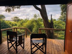 two chairs and a table on a deck with a tree at Buffalo Tented Camps in Mahango