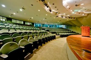 ein leeres Auditorium mit grünen Stühlen und einem Podium aus Holz in der Unterkunft Hotel Nacional Inn São José dos Campos in São José dos Campos