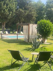 two chairs and a table in the grass near a pool at Gîte Les cyprès de l'ile in Avignon