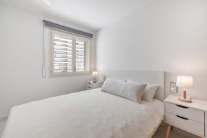 a white bedroom with a white bed and a window at Resguardo en la playa in Calafell