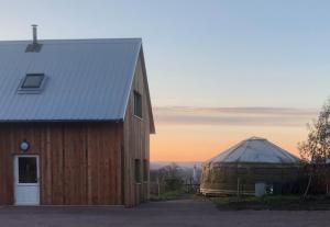a barn and a yurt with a sunset in the background at Les Jardins Vert Framboise yourte et chambres d'hôtes in Beaufour