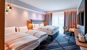 a hotel room with three beds and a desk at Premier Inn München Airport Süd in Hallbergmoos