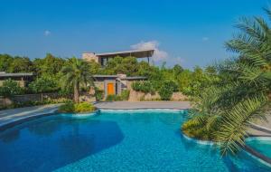 a swimming pool in front of a house with a palm tree at The Forest Chapter by Sayaji Sasan Gir in Chitrod