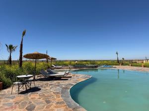 a swimming pool with chairs and an umbrella and a table at Dar Diyafa Marrakech in Maout