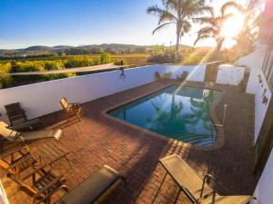 a swimming pool on a brick patio with chairs and the sun setting at Merwenstein - Farm House, Cottages, Studio-Units in Bonnievale