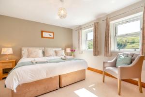 a bedroom with a bed and a chair and two windows at 3 Bed in Gunnerside oc-ds097 in Gunnerside
