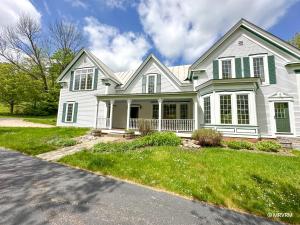 a white house with green shutters on a street at West Hill Farmhouse in Warren