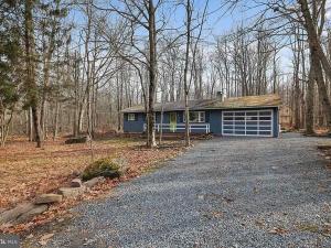 a blue house with a garage in the woods at Firepit Game Room Seclusion and More in Locust Lakes Village
