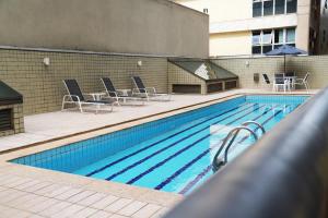 a swimming pool with chairs and a table and a building at Promenade Pancetti Belo Horizonte in Belo Horizonte