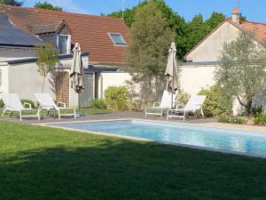 a pool with chairs and umbrellas next to a house at Le cheval bleu in Larçay