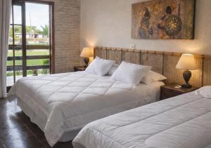 two beds in a hotel room with white sheets at Hotel Cumuruxatiba in Cumuruxatiba