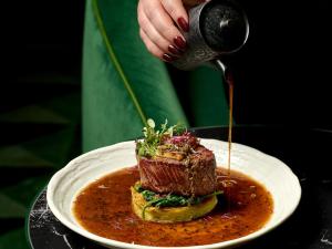 a person is pouring sauce onto a plate of food at Falkensteiner Boutique Hotel Prague in Prague