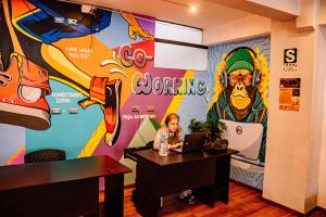 a woman sitting at a table with a laptop in front of a mural at Magic Packer Hostel in Cusco