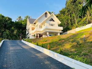 a white house on a hill with a road at Trinity Villa Home Stay in Idukki
