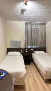 two beds in a room with a table and a window at Cit'Hotel Primo Colmar Centre in Colmar