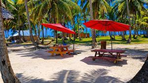 two picnic tables and red umbrellas on a beach at camping eco demar achu in Cayos Los Grullos