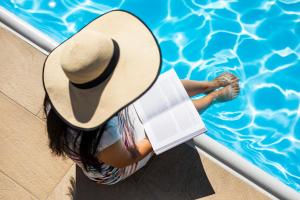 a woman wearing a hat reading a book next to a swimming pool at Hotel Markushof - Adults only in Auer
