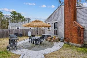 a patio with a table and a straw umbrella at The Coast: Cozy Cape Escape in Dennis Port in Dennis Port