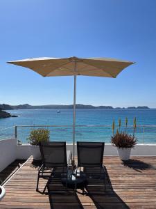two chairs and an umbrella on a wooden deck with the ocean at Carabela in Paguera