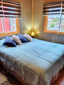 a bed with blue pillows in a bedroom with windows at Casa kumey in Puerto Varas