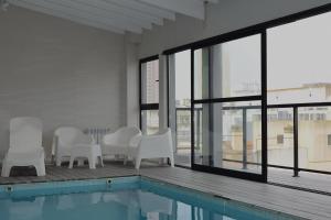 a pool with white chairs and a table and windows at C&R Departamentos y Hoteles in Mar del Plata