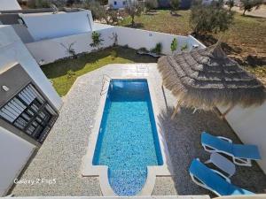 a swimming pool with a straw umbrella and some chairs at villa amani in Al Maqārisah
