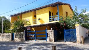 a yellow house with a blue fence in front of it at Pousada Montreux in Praia do Forte