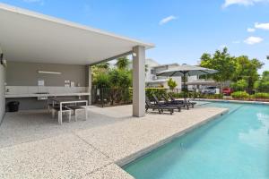 a swimming pool with a table and chairs next to a house at Direct Collective - Breeze on Brightwater in Mooloolaba