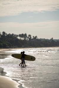 two people walking on the beach with a surfboard at Southbeach Weligama in Weligama