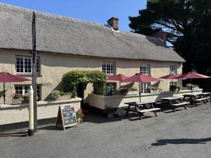 a building with tables and umbrellas in front of it at Drewe Arms Bunk Rooms in Drewsteignton