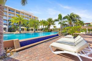a pool at a resort with lounge chairs and palm trees at Le Vent Eagle Beach Condos by Bocobay Aruba in Palm-Eagle Beach