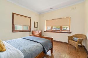 a bedroom with a bed and a chair and two windows at Red Brick Beauty - Central Cottage in Albury