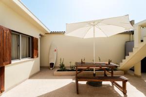 a patio with a table and an umbrella and a surfboard at Casa da Areia - by RowdHouses - Private Beach Access in Praia da Barra