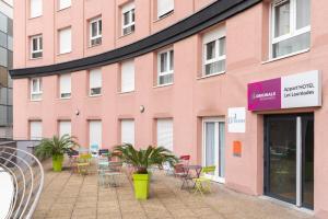 a pink building with tables and chairs in front of it at The Originals Residence Appart'Hôtel Lauréades Clermont-Ferrand Centre Jaude in Clermont-Ferrand