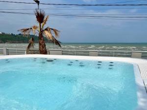 a swimming pool with a palm tree and the ocean at Beach house Maison de plage les pieds dans l eau in Plérin