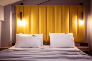 a bed with two pillows and a yellow wall at Old Cinema Suites - Stylishly Decorated Retreat with Pool or Jacuzzi by the Sea in the Heart of Laganas Βy Villa Mana Gers in Laganas
